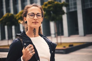 nice young woman with piercing glasses tattoo her neck is posing photographer street